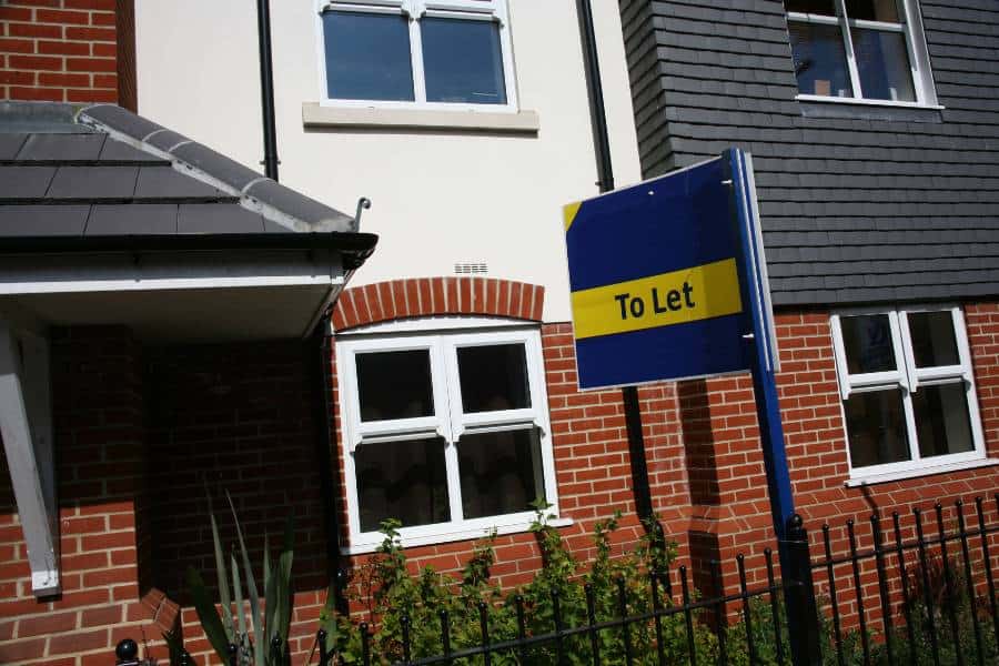 A terraced property with a to let sign - Couple using a laptop in their rented property - Assets For Life