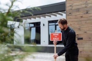 Man putting a for sale sign outside a property - Assets For Life