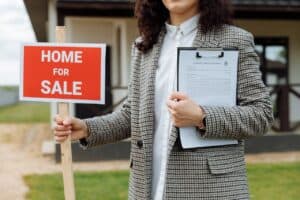 Woman holding a for sale sign outside a home - Assets For Life